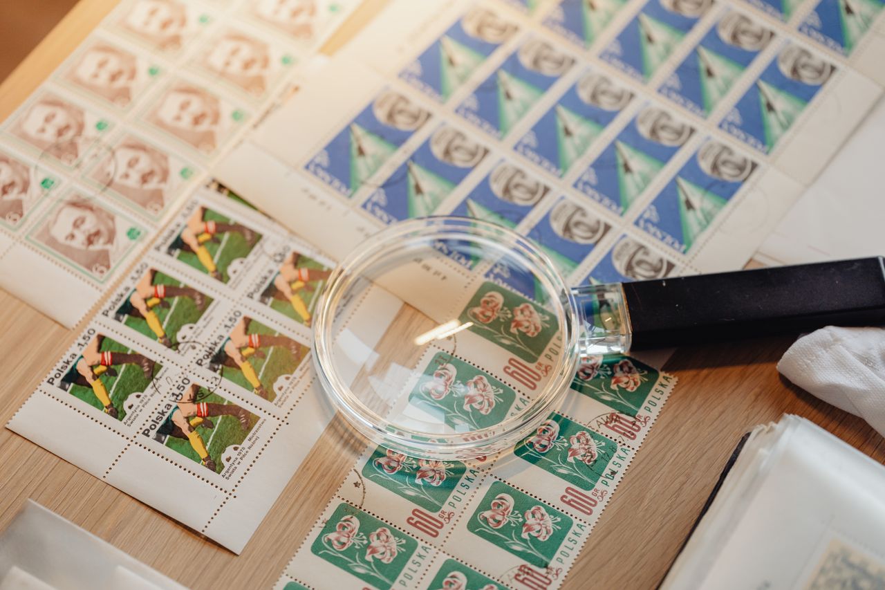 A detailed view of a vintage postage stamps collection accompanied by a magnifying glass on a wooden surface.